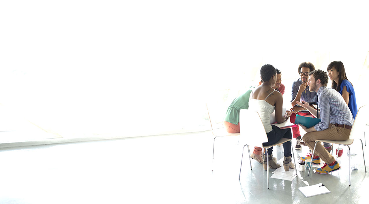 A group of male and female young professionals sit together at a table and collaborate.